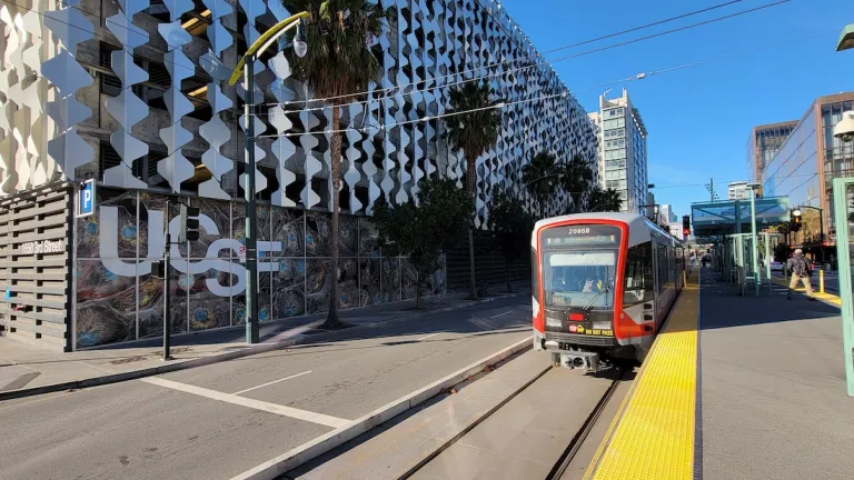 A Muni light rail train at a stop across the street from a UCSF building