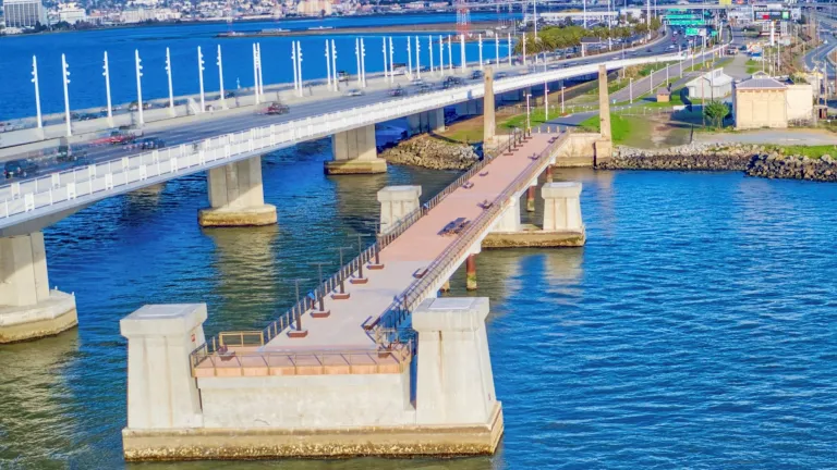 An observation pier juts into the San Francisco Bay from the Oakland shoreline, with the touchdown of the Bay Bridge East Span in the background.