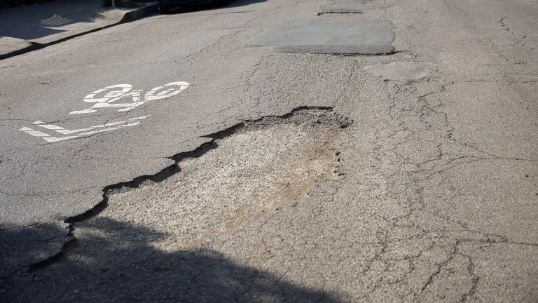 Potholes in the pavement next to a sharrow bike marking.