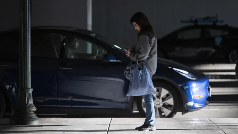 A woman looking at her phone next to a vehicle passenger pickup area at MacArthur BART station.