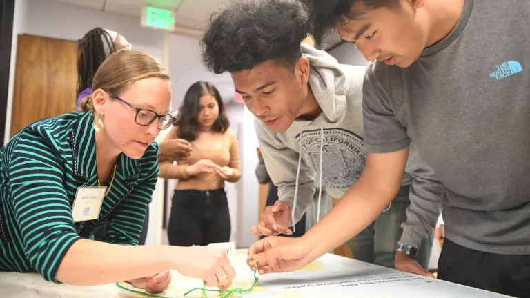 Two teenagers work on a mapping activity at an engagement event while a woman looks on.