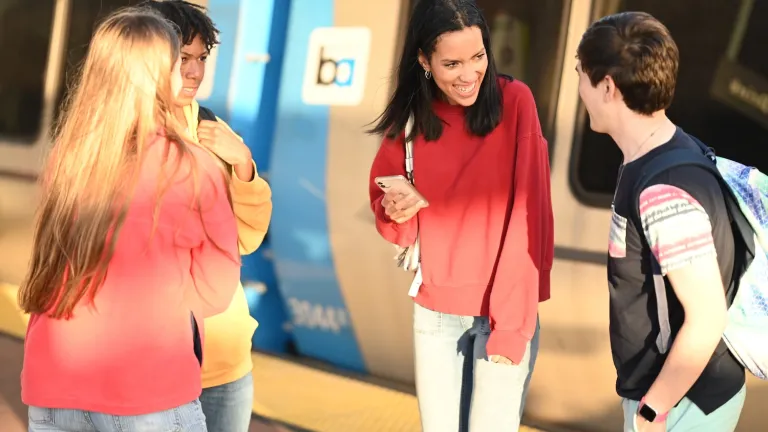 A group of young people are waiting on a BART train platform with a train in the background. 