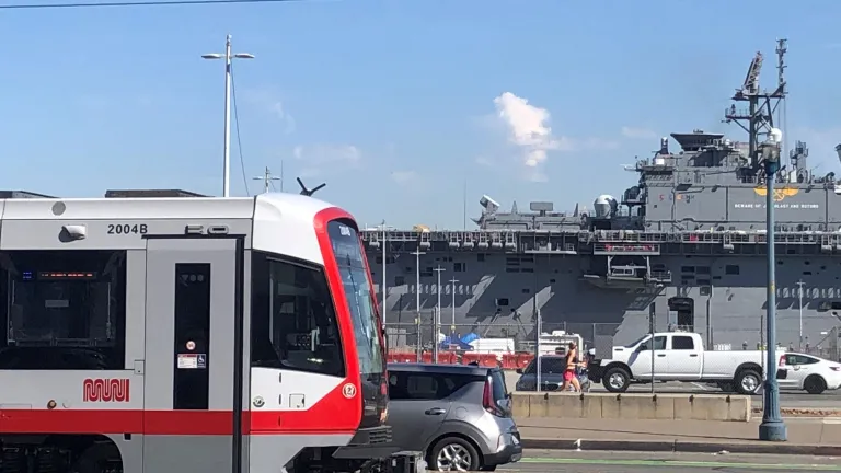 A Muni train passes by a US Navy ship docked in San Francisco.