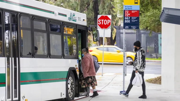 A woman boards an AC Transit bus at El Cerrito del Norte BART station while a man waits to board behind her.