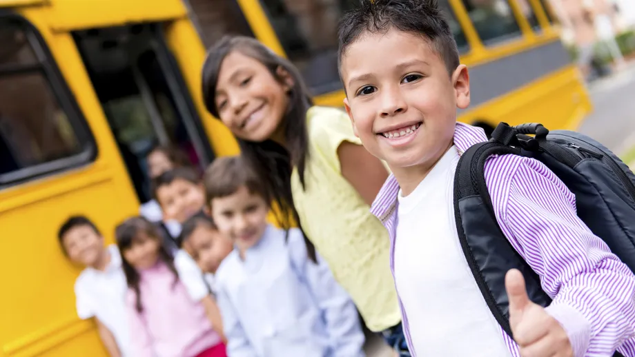 Elementary school students line up in front of a yellow school bus