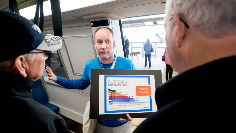 man talking to commuters inside train