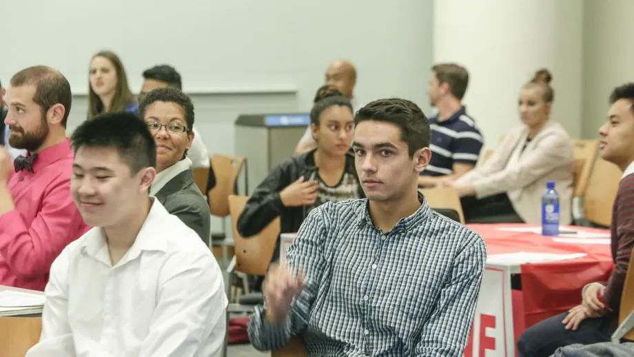 young adults sitting at tables listening to speakers