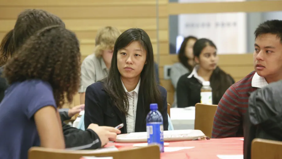 young adults sitting at tables listening to speakers