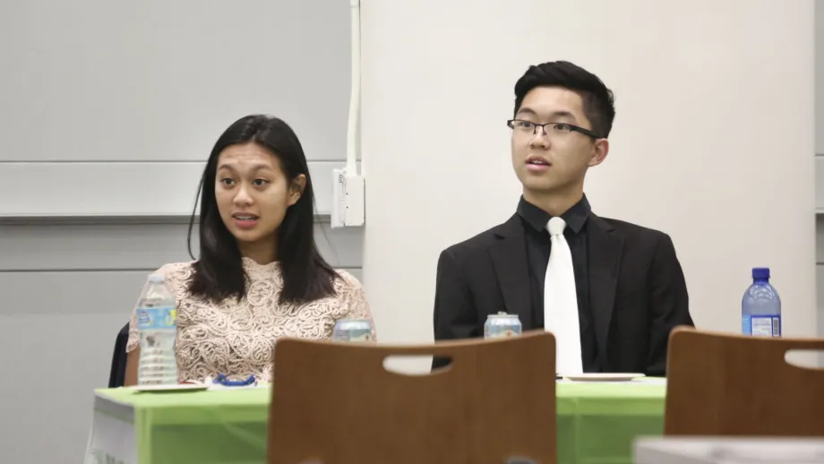 young adults sitting at tables listening to speakers