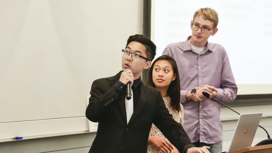 young adult holding microphone next to a podium