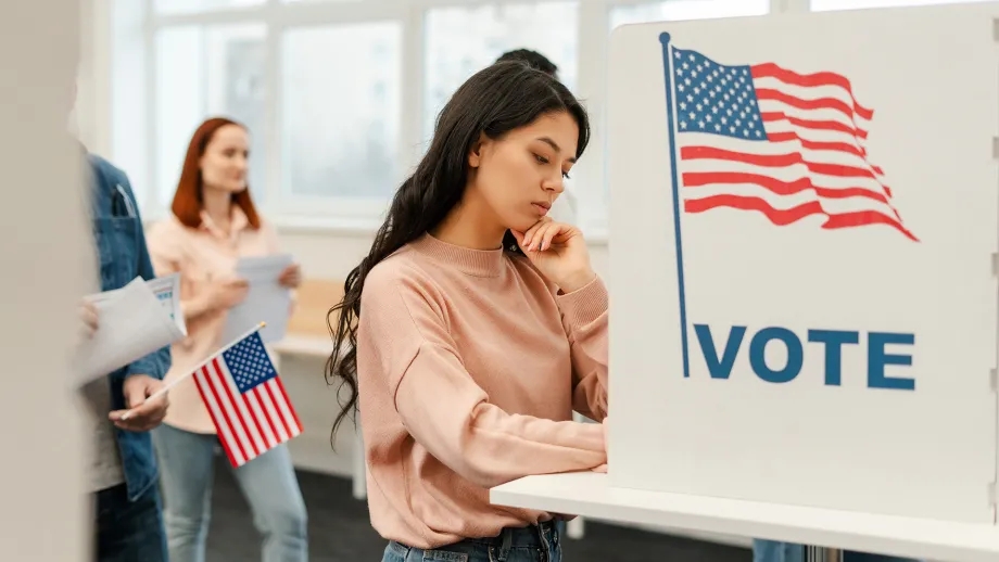 A woman contemplates her choices at a voting booth.