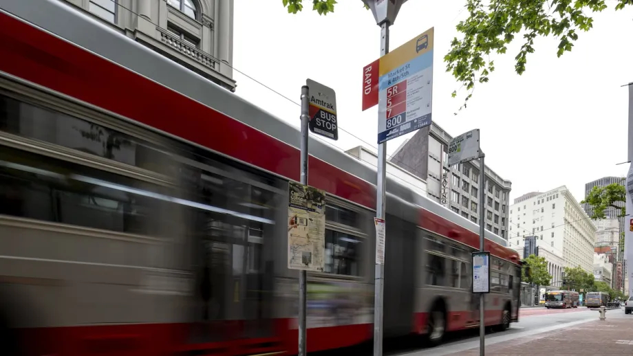 New test bus stop signs are in the foreground while a Muni bus drives past the signs on San Francisco's Market St. in the background