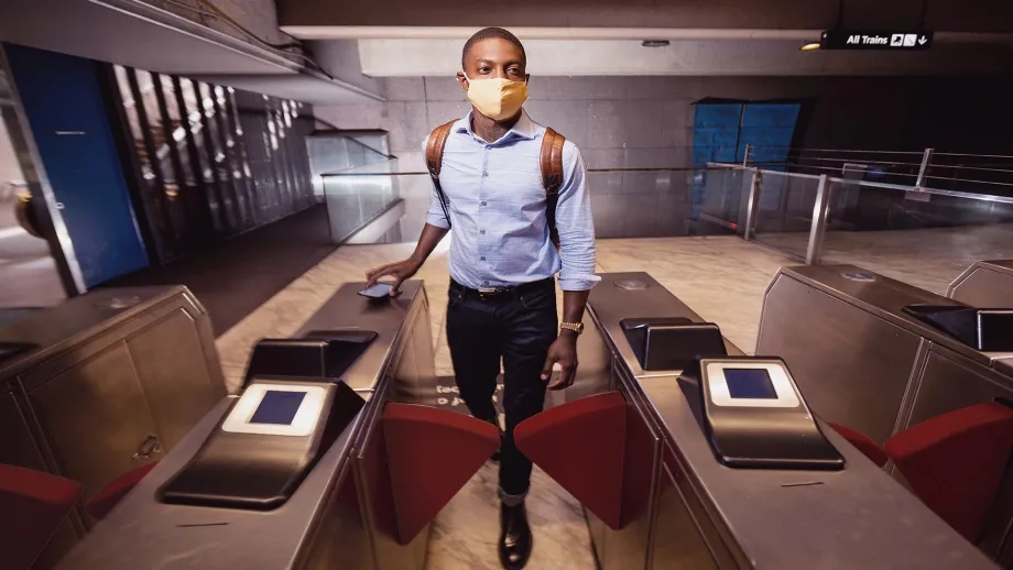A man wearing a mask taps his mobile phone to pay for his ride at a BART fare gate.