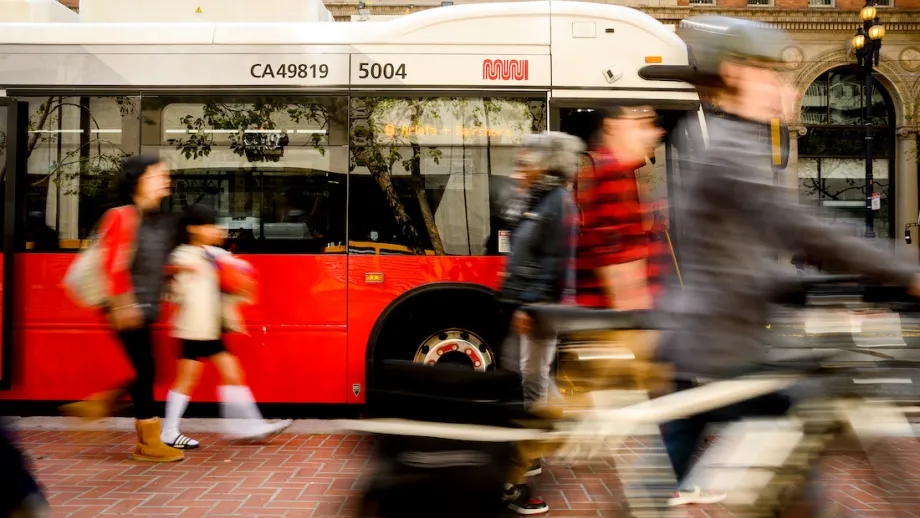 People on the sidewalk walking past a Muni bus in San Francisco. 
