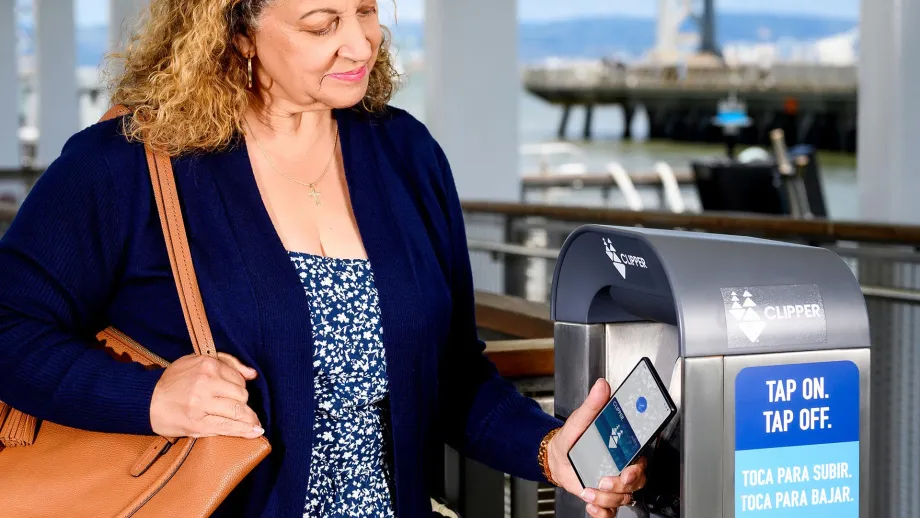 A smiling woman pays for transit with Clipper on her phone.