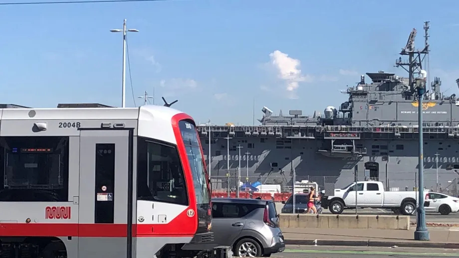 A Muni train passes by a US Navy ship docked in San Francisco.