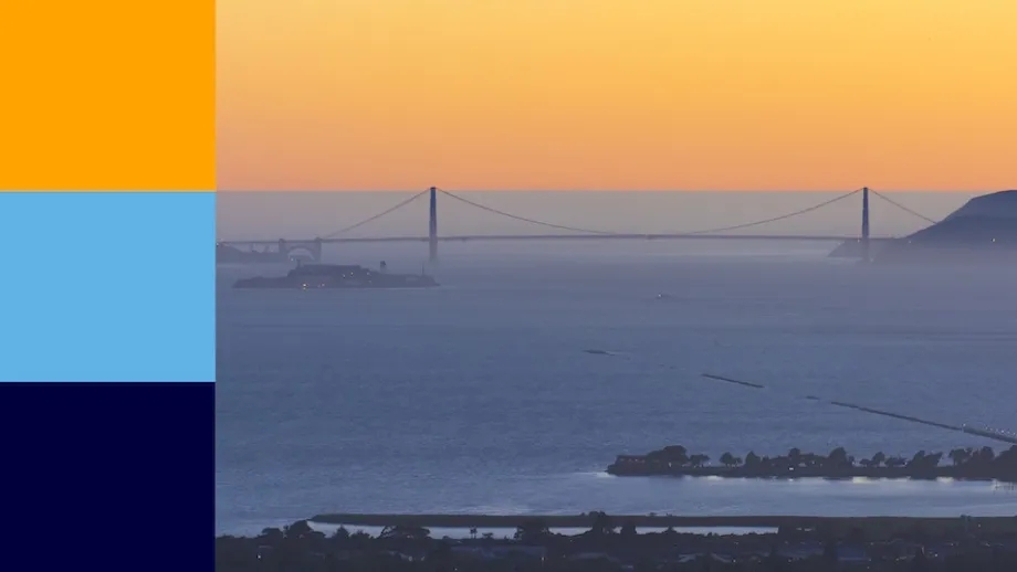 A westward-looking sunset view of the Golden Gate Bridge, with colors of gold, sky blue and dark blue.