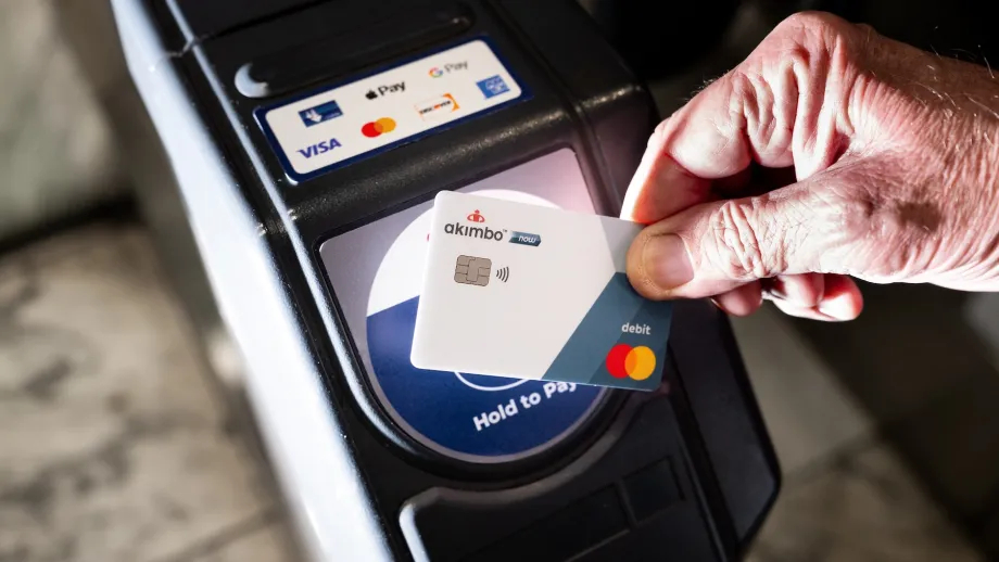 A hand holds a credit card against a sensor to pay for transit.